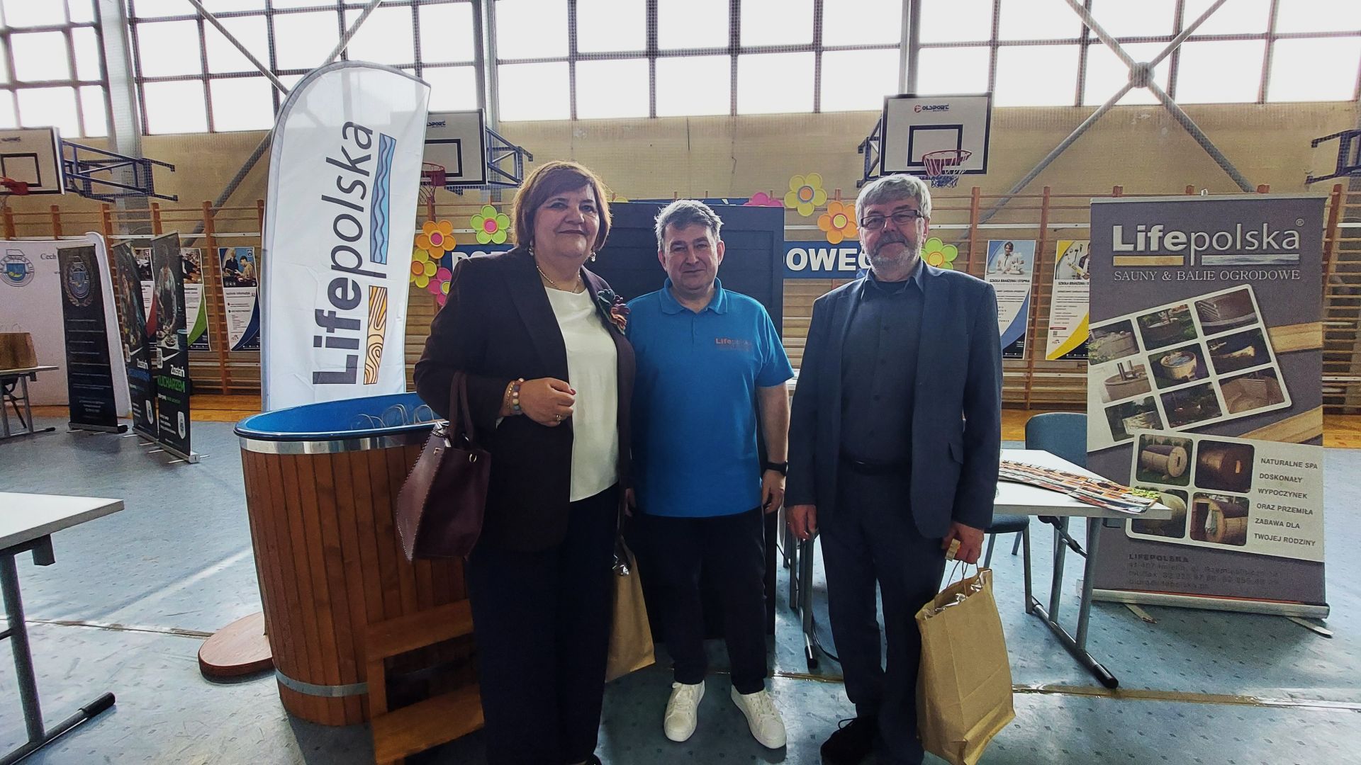 Zdjęcie trzech osób stojących  na tle banerów reklamowych